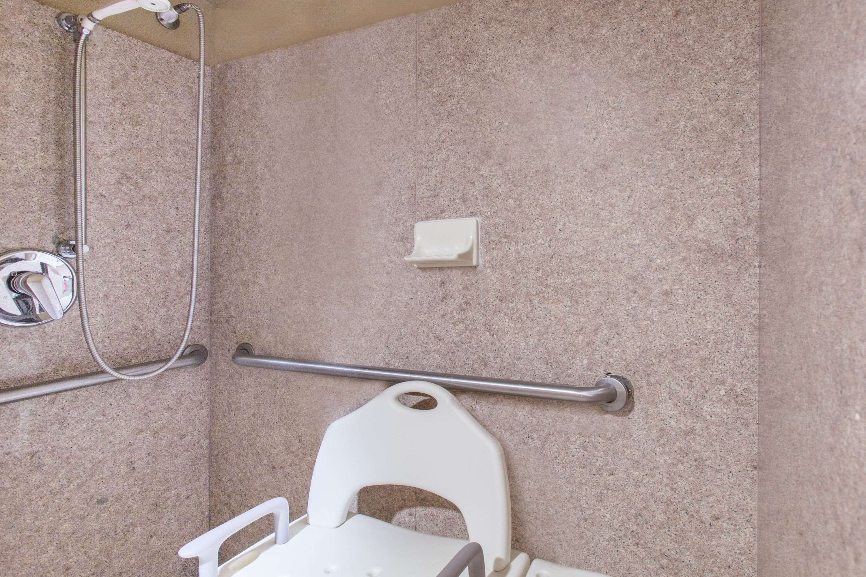 Une salle de bain avec douche, barre d’appui et toilettes blanches.