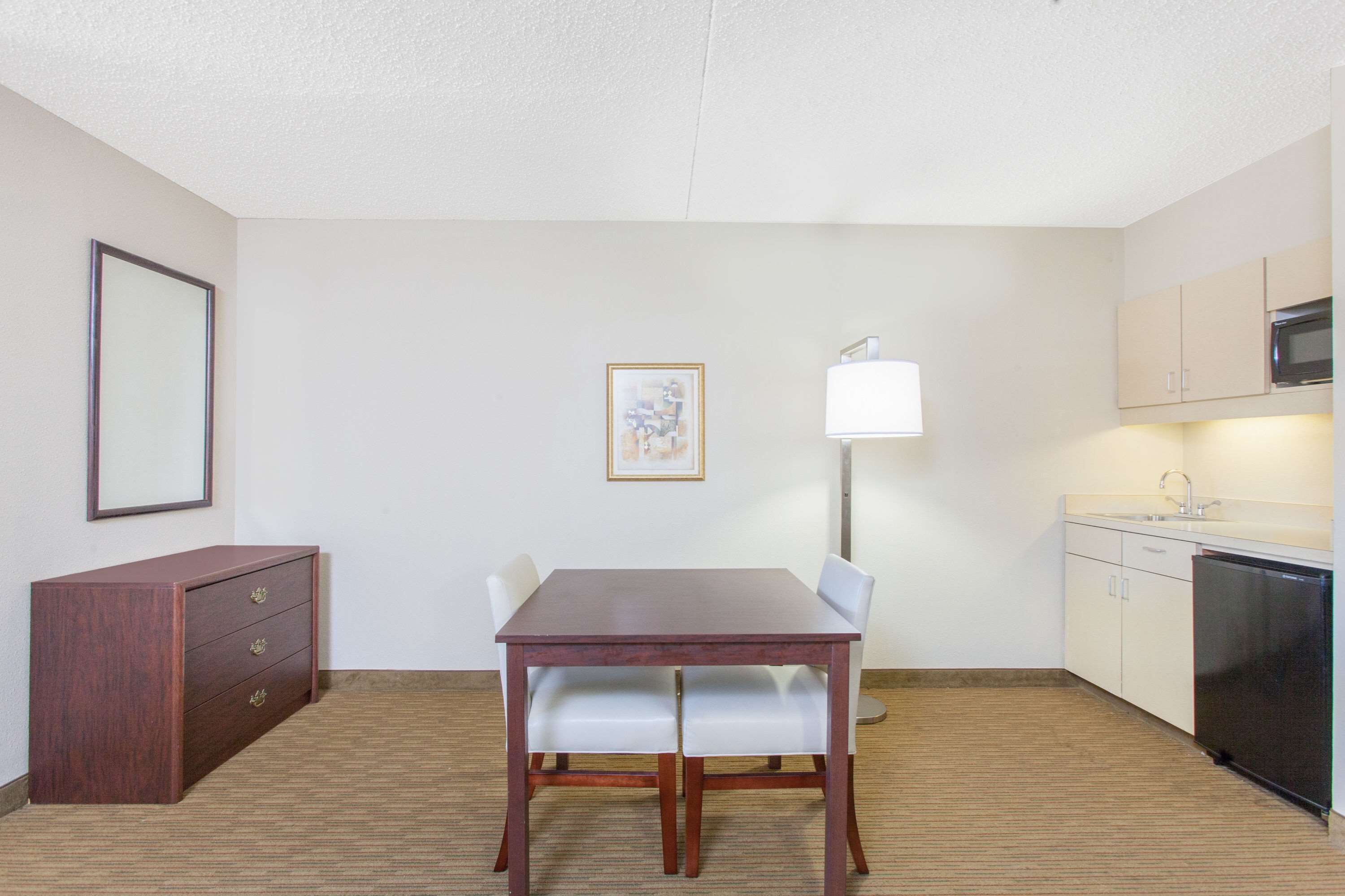 A small, clean room with a wooden table, two chairs, a cabinet, a lamp, and a microwave.
