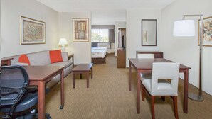 A hotel room with a bed, a sofa, a desk, a chair, a lamp, and artwork on the walls. - Hawthorn Suites by Wyndham Midwest City Tinker AFB (Midwest City)