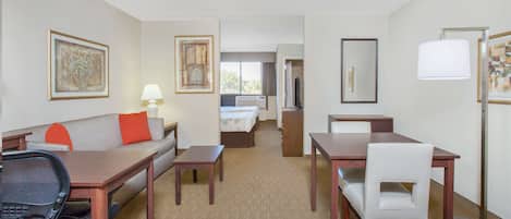 Habitación de hotel con cama, sofá, escritorio, silla, lámpara y obras de arte en las paredes.