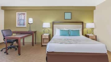 Habitación de hotel con una cama grande, un escritorio, dos lámparas de noche, una silla y un cuadro enmarcado en la pared.