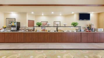 A reception area with a wooden counter, a television mounted on the wall, and various amenities like a coffee machine, fruit bowl, and framed pictures.