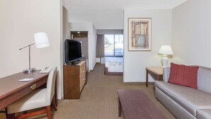 A hotel room with a desk, chair, television, sofa, and a small table with a lamp. - Hawthorn Suites by Wyndham Midwest City Tinker AFB (Midwest City)