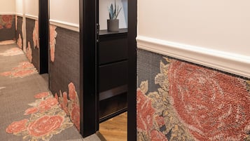 Un pasillo de hotel con piso alfombrado, pared con estampado floral y una puerta negra, con un cartel que indica la habitación número 304.