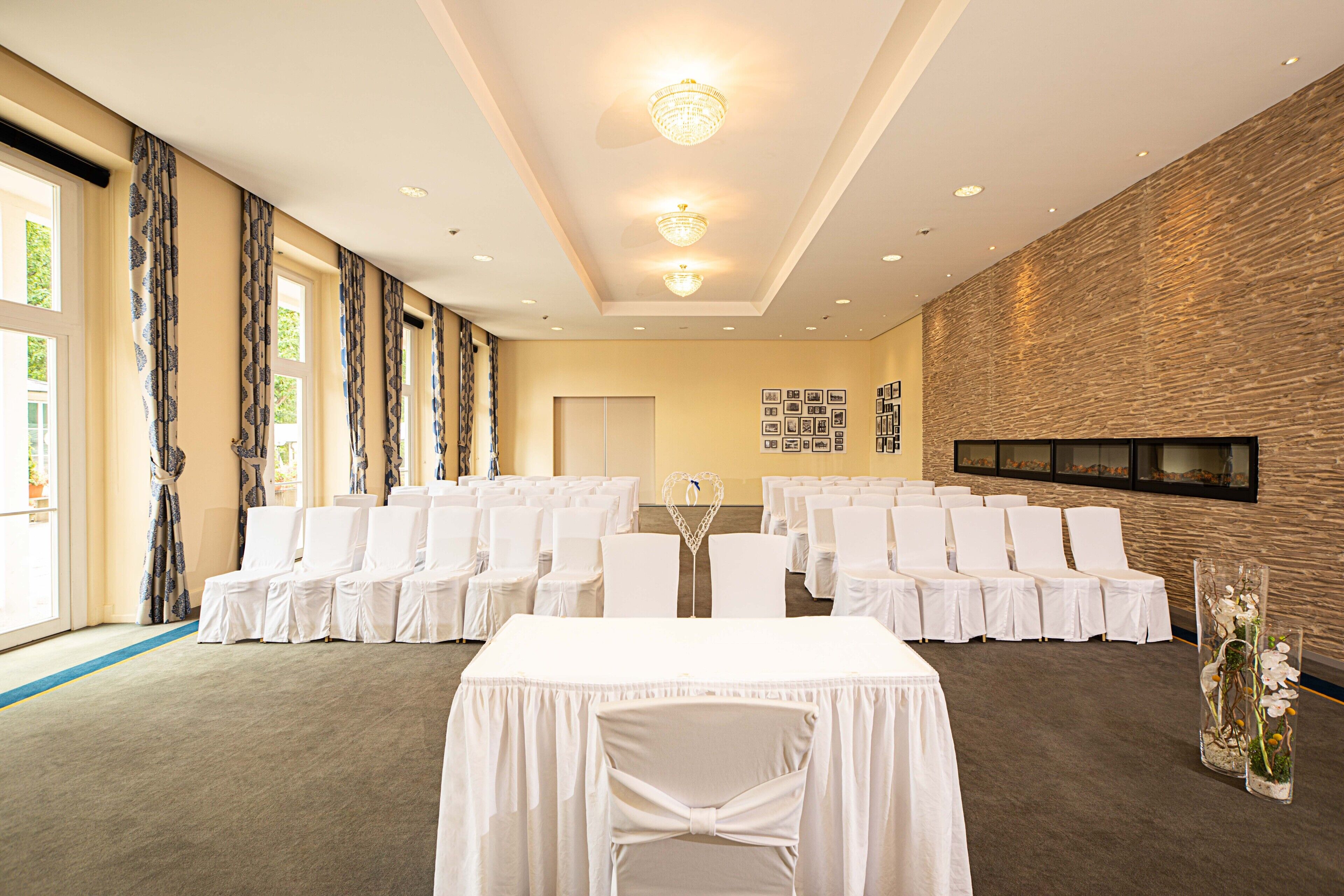 A conference room with rows of white chairs, a central table, and a chandelier.