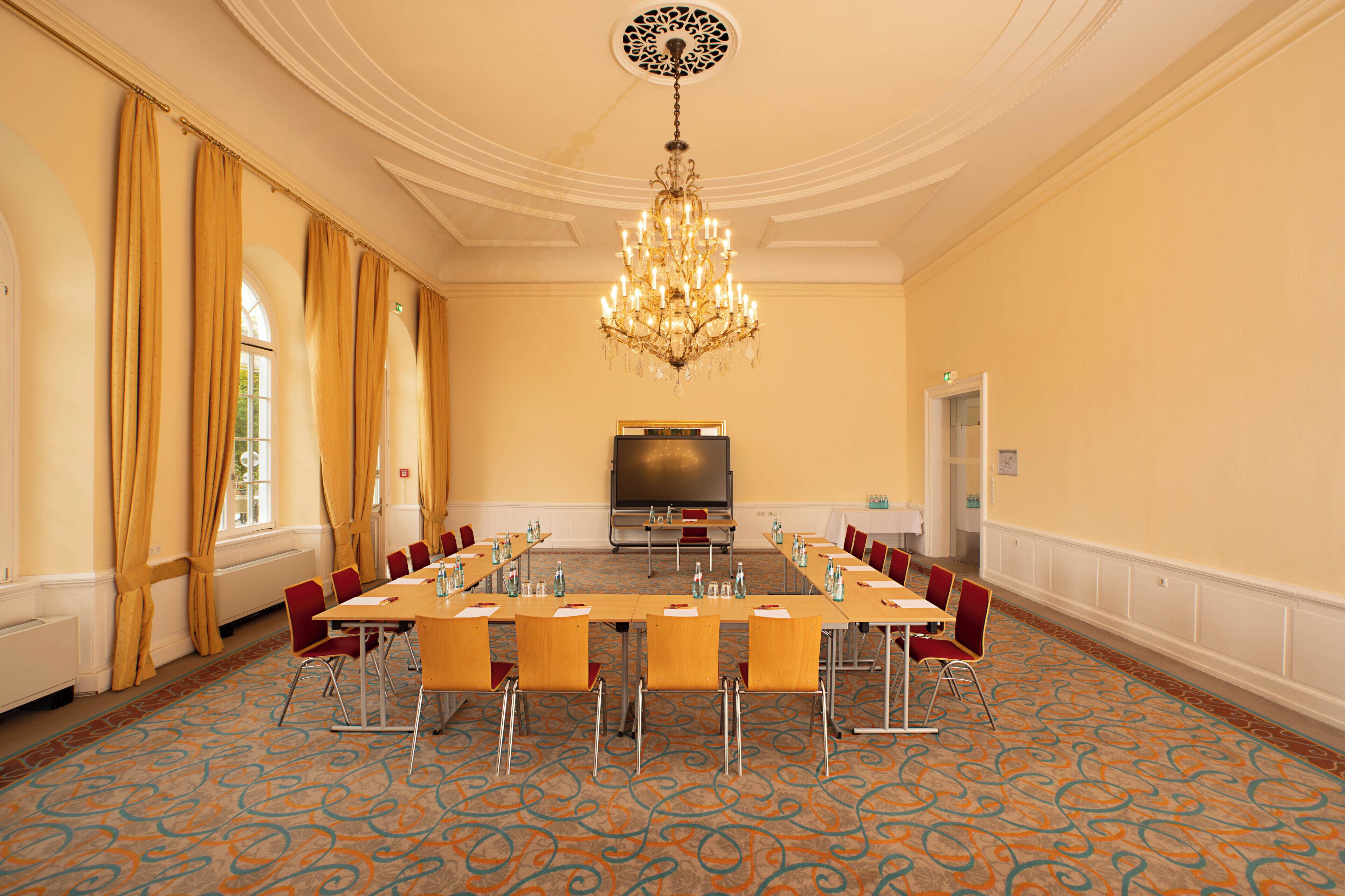 A conference room with a long table, chairs, a projector screen, and a chandelier.