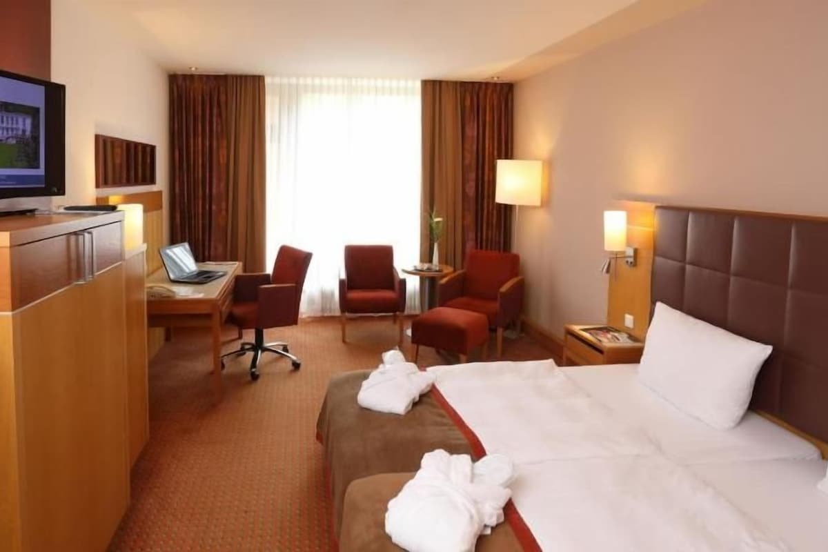 Ein Hotelzimmer mit Bett, Schreibtisch, Stuhl, Fernseher und einem Fenster mit Vorhängen.