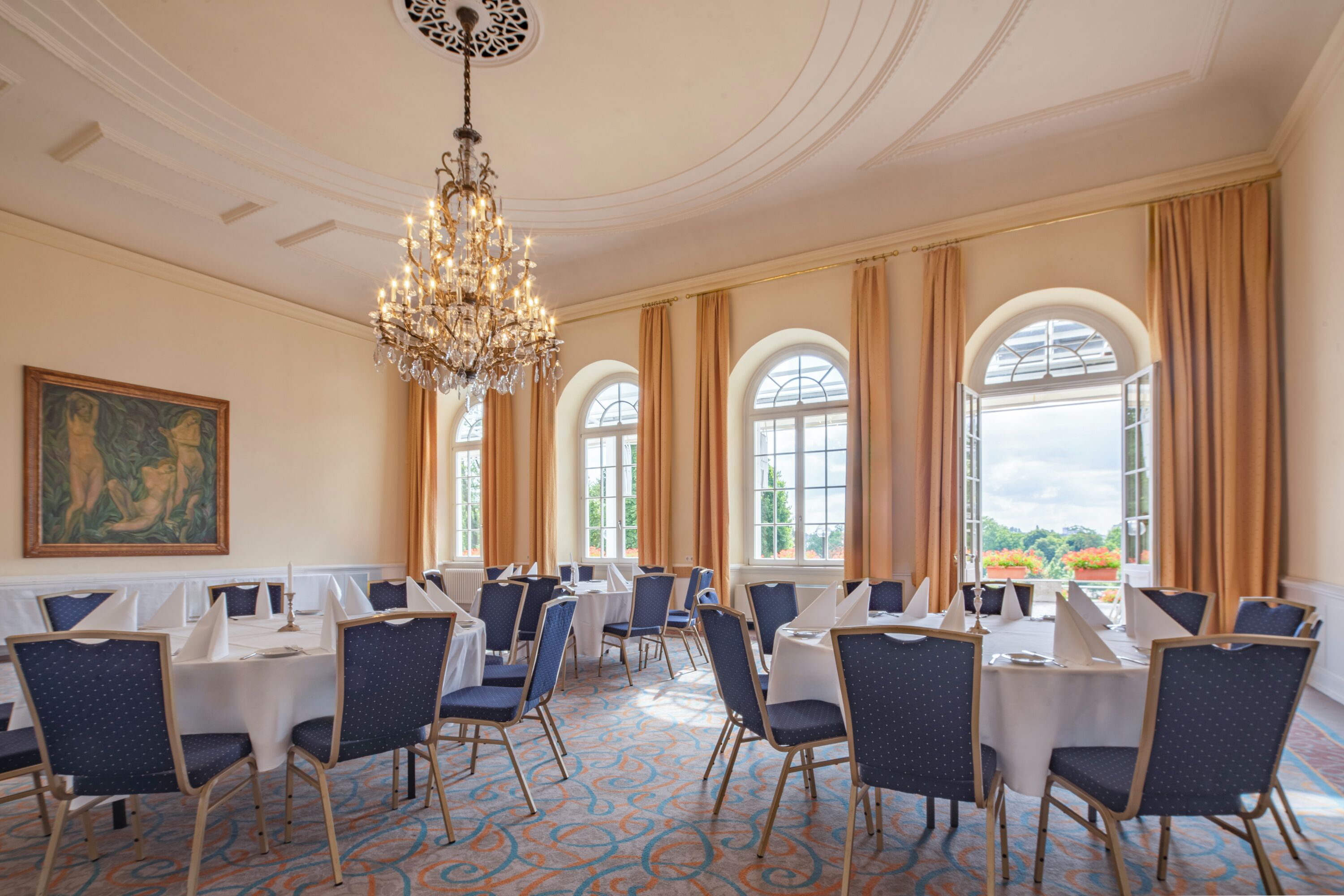 A conference room with round tables, blue chairs, and a chandelier.