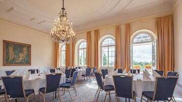 A conference room with round tables, blue chairs, and a chandelier.