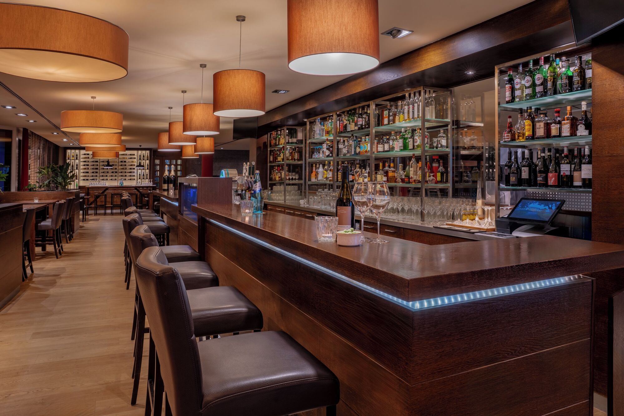 Un'area bar con banconi in legno, sgabelli da bar in pelle e una selezione di bottiglie di liquore sugli scaffali.