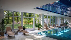 Une piscine intérieure moderne, dotée de grandes fenêtres, de chaises longues et de plantes en pot.