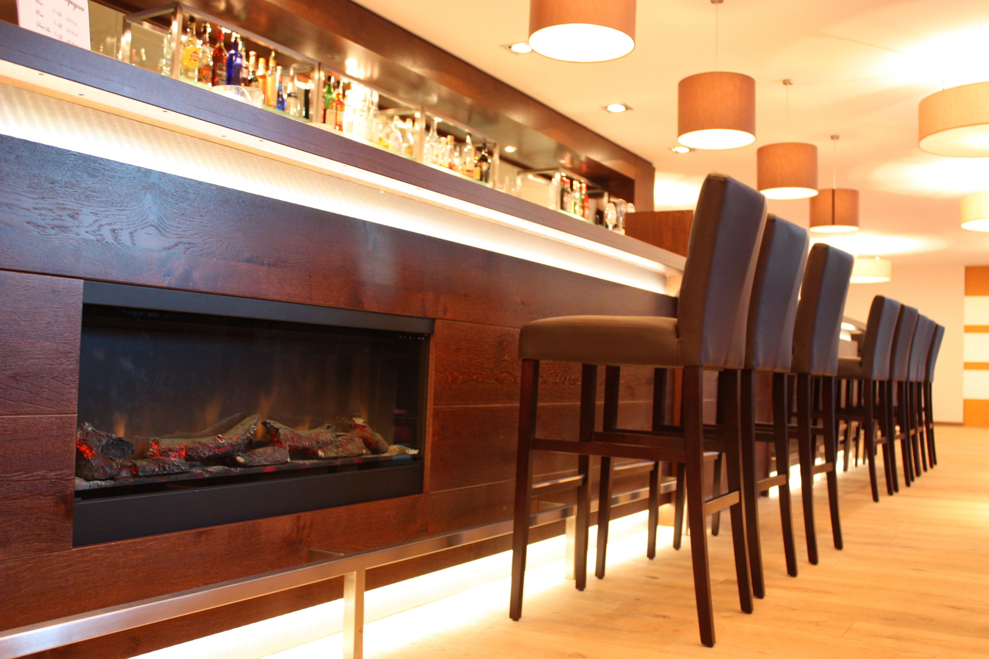 Zona de bar con chimenea, mostrador de madera y múltiples sillas.