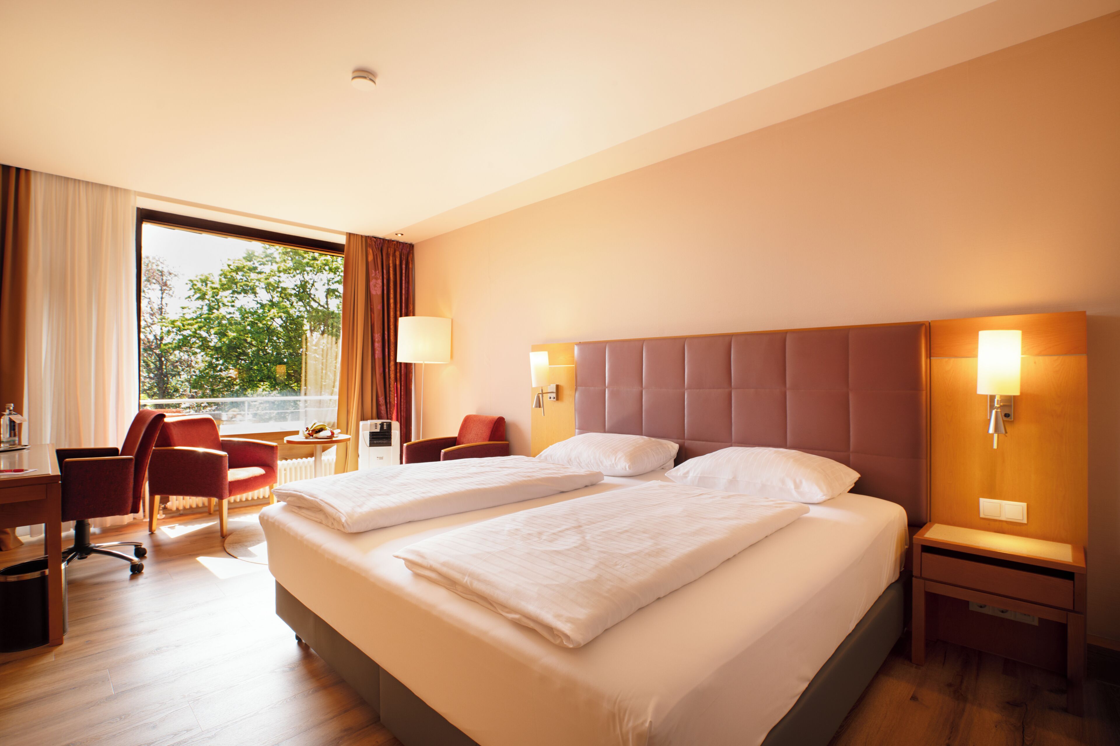 Ein Hotelzimmer mit zwei Betten, einem Schreibtisch, einem Stuhl und einem Fenster mit Vorhängen.