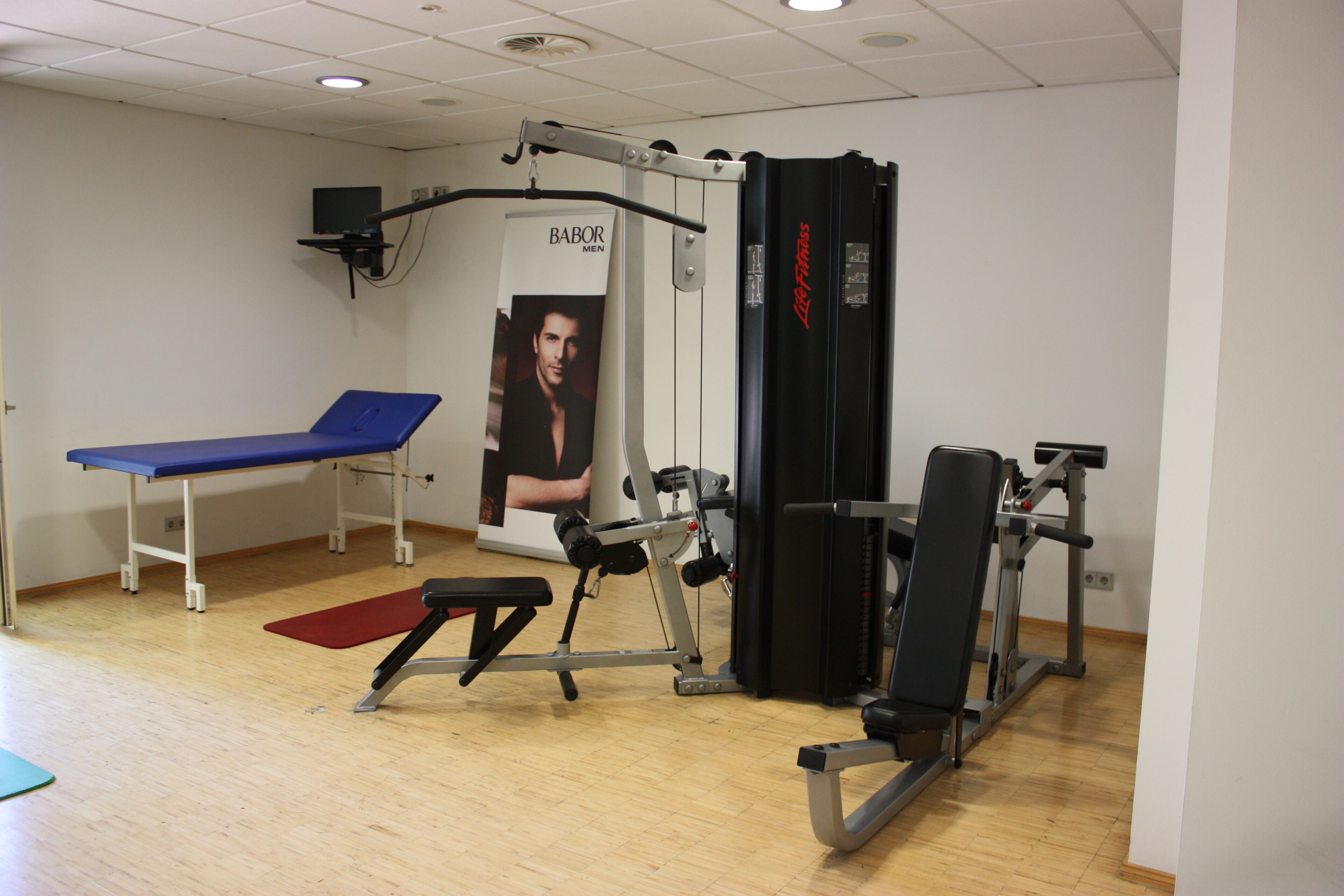 A gym with exercise equipment, a blue bench, and a red mat.