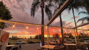 An outdoor seating area with tables and chairs, palm trees, and a sunset view. - Crowne Plaza Perth by IHG (East Perth)