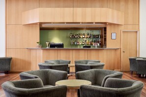 A bar area with a wooden counter and shelves of bottles, surrounded by grey upholstered chairs and a small round table.