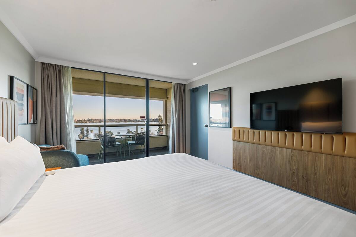 A hotel room with a large bed, a television, a balcony with a view, and a wooden headboard.