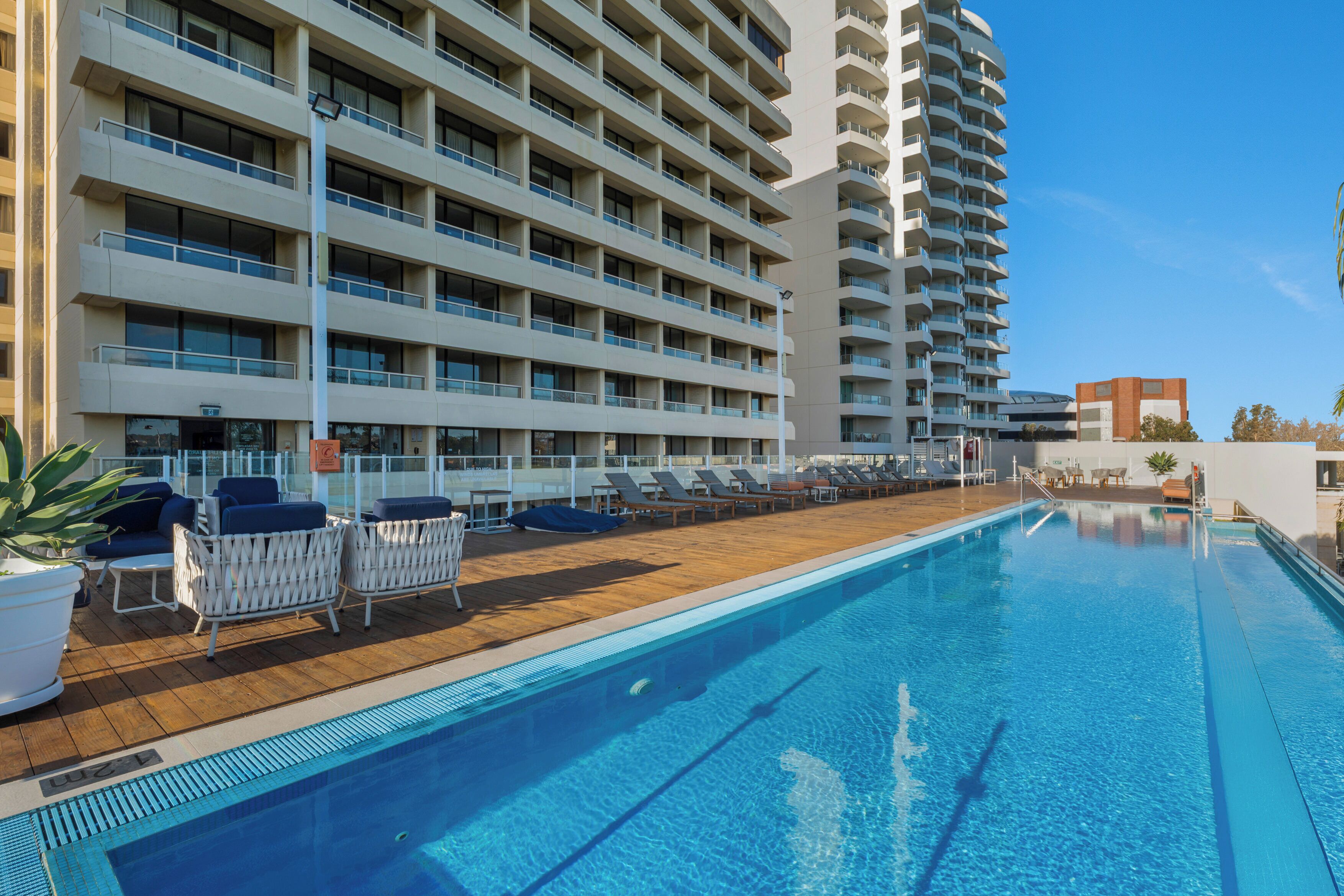 A hotel with a swimming pool, multiple balconies, and lounge chairs.