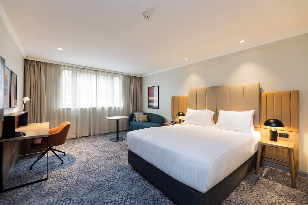 A hotel room with a large bed, a desk with a chair, a small round table, and a sofa.