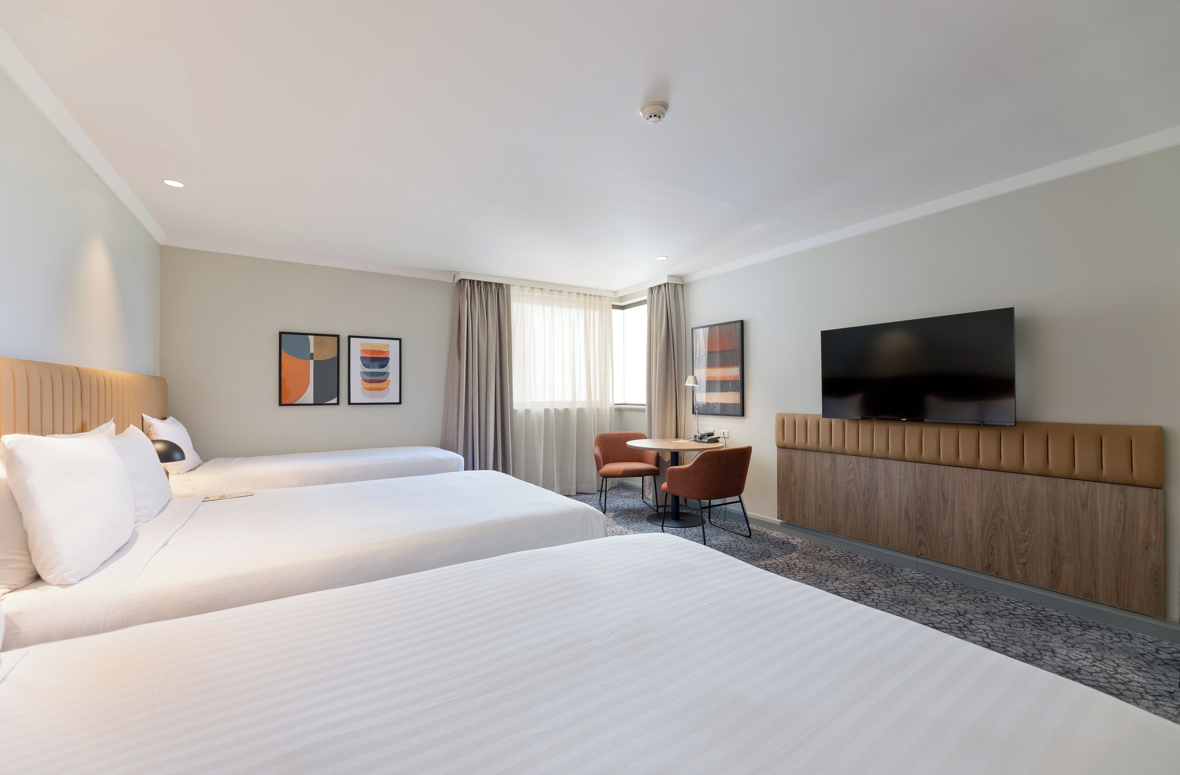 A hotel room with two beds, a desk, a chair, a television, and artwork on the walls.