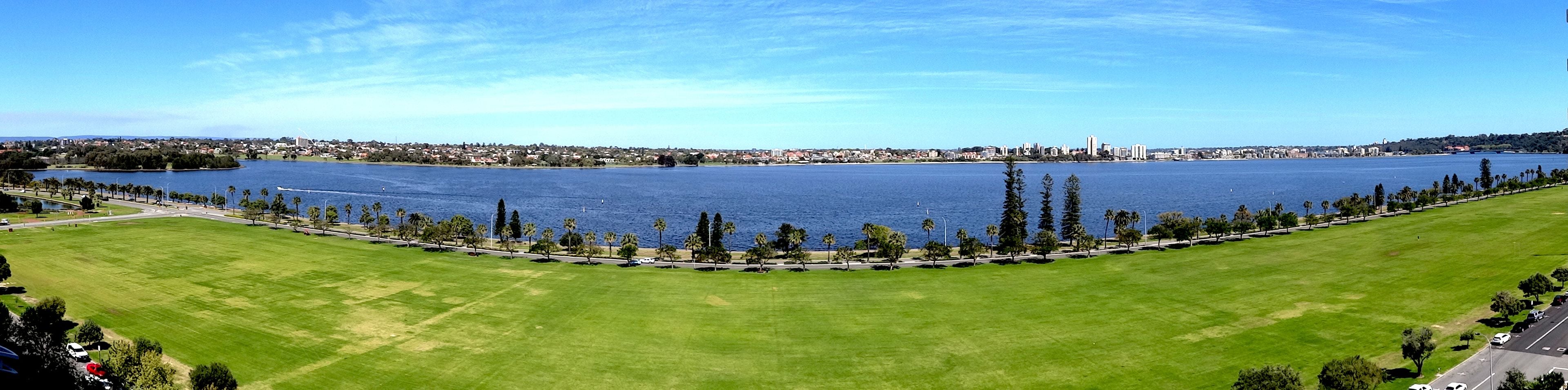 A large, open grassy area with a body of water and a distant cityscape.