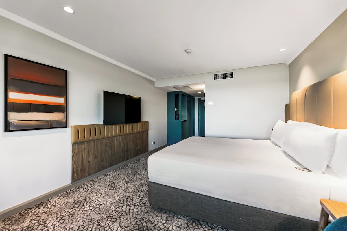 A modern hotel room with a large bed, a flat-screen TV mounted on the wall, and a unique patterned carpet.