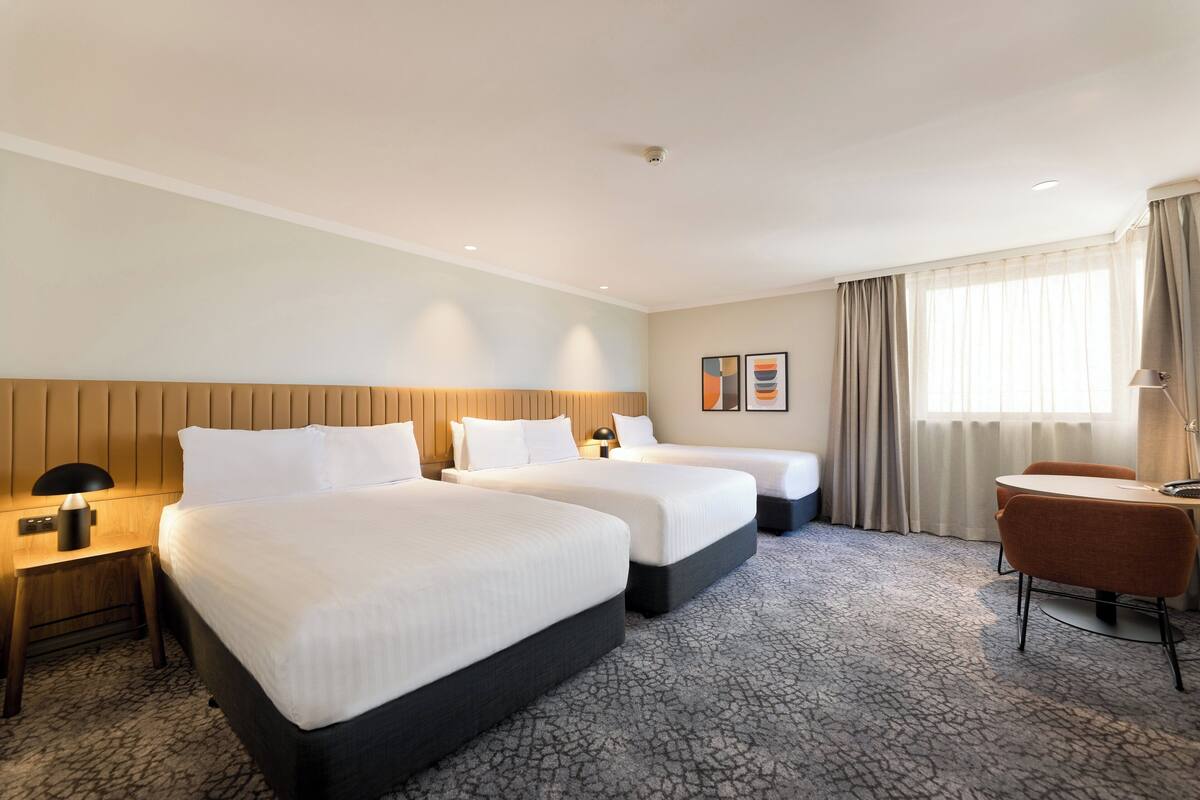 A hotel room with two beds, a desk, a chair, and a window with curtains.