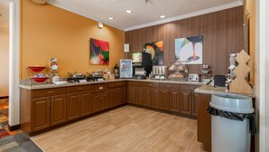 A kitchen with wooden cabinets, a coffee machine, a microwave, and a trash can. - Wingate by Wyndham Great Falls (Great Falls)
