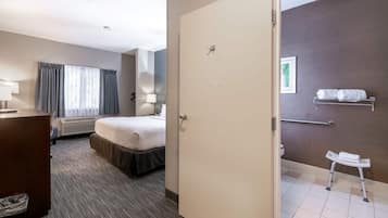 A hotel room with a bed, a desk, a chair, a window with curtains, a wall-mounted towel rack, and a small step stool.