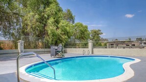 Una piscina con una escalera de metal, rodeada por un suelo de hormigón y una valla de metal.
