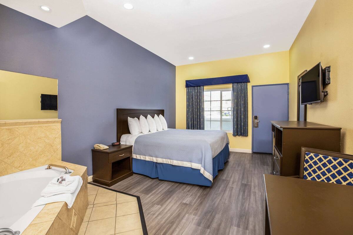 A hotel room with a bed, a desk, a chair, a TV, and a window with curtains.