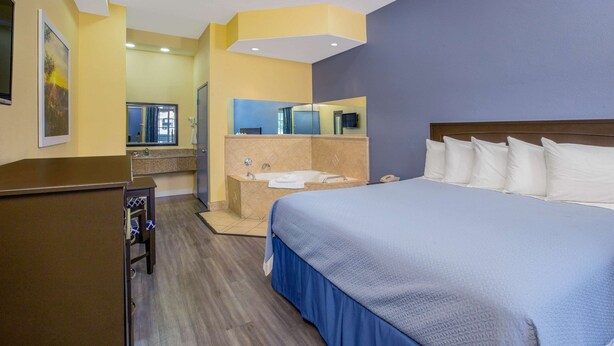 Habitación de hotel con una cama grande, baño con bañera y escritorio con silla.