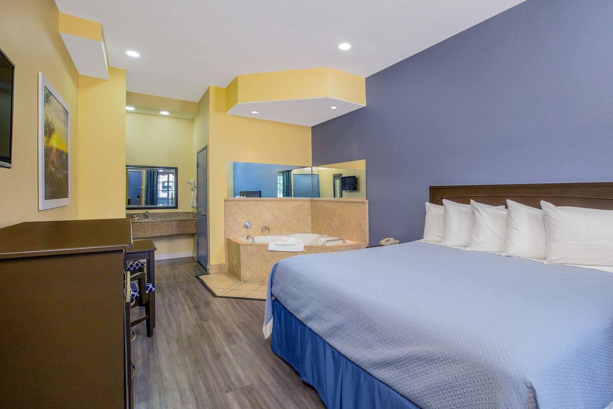 A hotel room with a large bed, a bathroom with a bathtub, and a desk with a chair.
