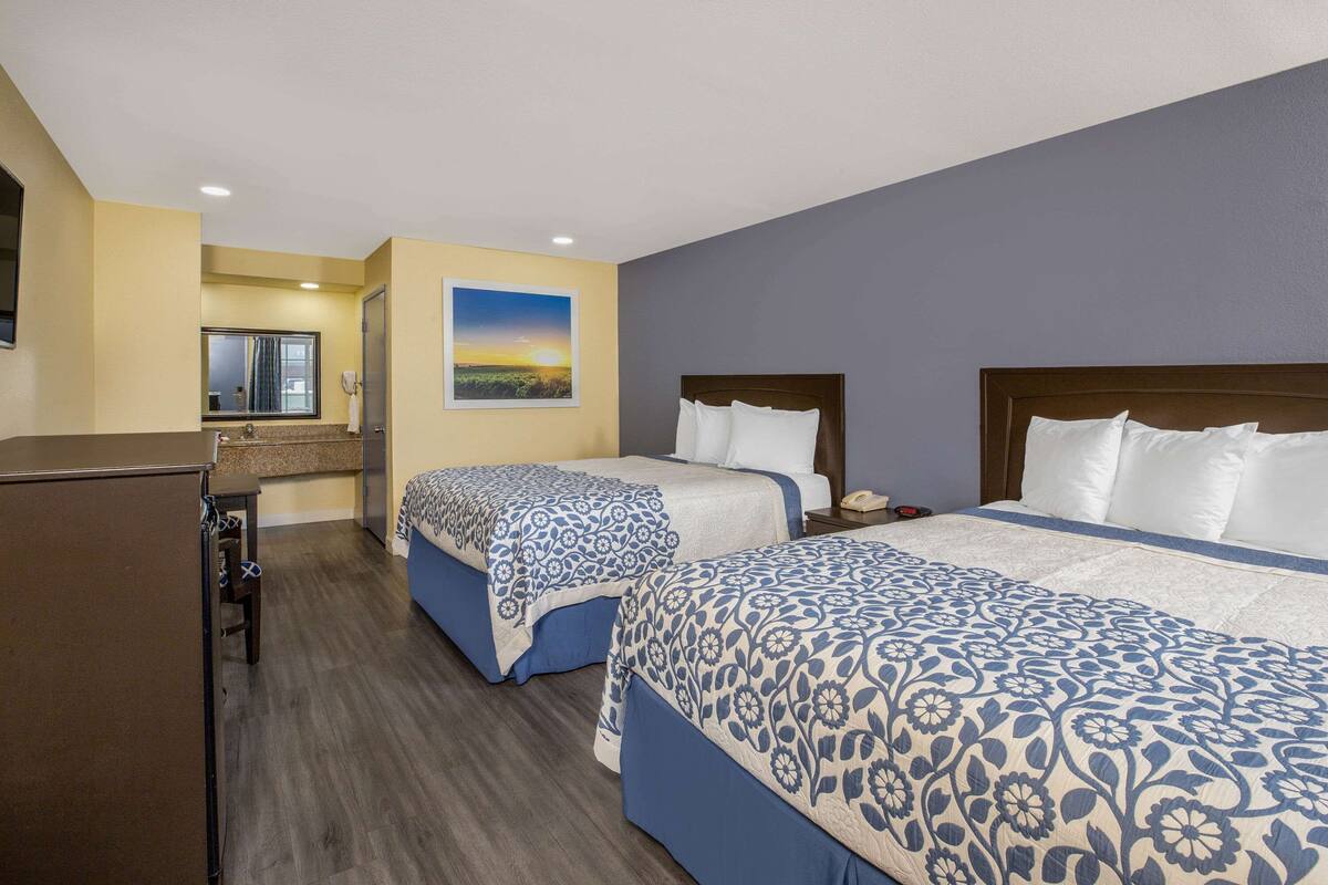 A hotel room with two beds, a desk, a mirror, and a painting of a sunset.
