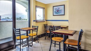 Un restaurante con varias mesas y sillas, ventanas amplias y un cuadro en la pared.