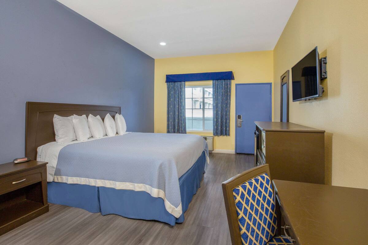 A hotel room with a large bed, a desk, a chair, a TV, and a window with curtains.