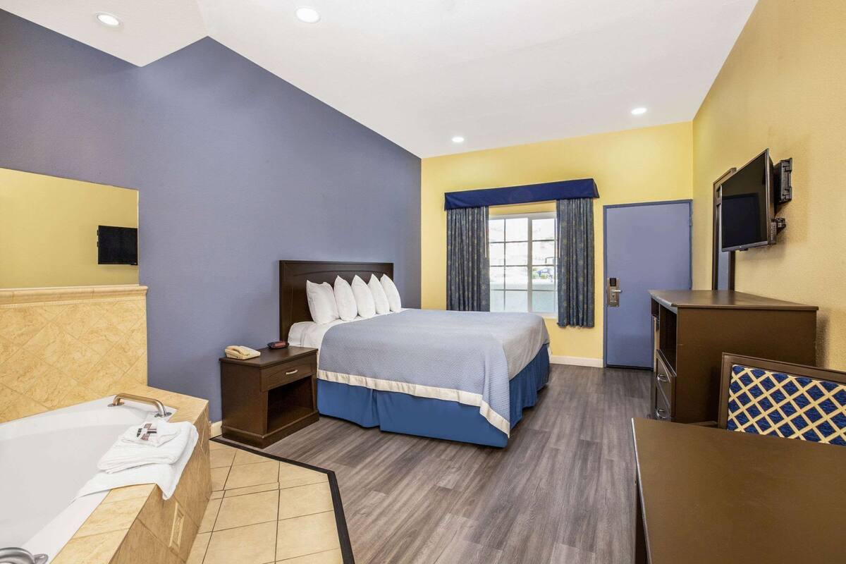 A hotel room with a bed, bedside table, TV, and a bathroom with a bathtub.