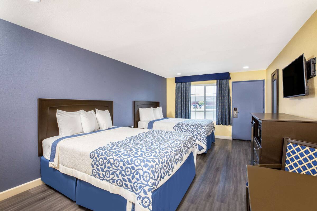 A hotel room with two beds, a TV, a desk, and a window with curtains.