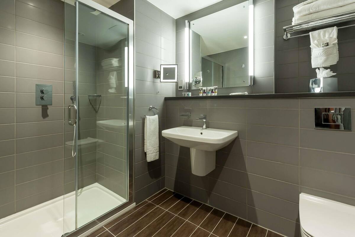 A modern bathroom with a glass-enclosed shower, a white sink, and a large mirror above the sink.