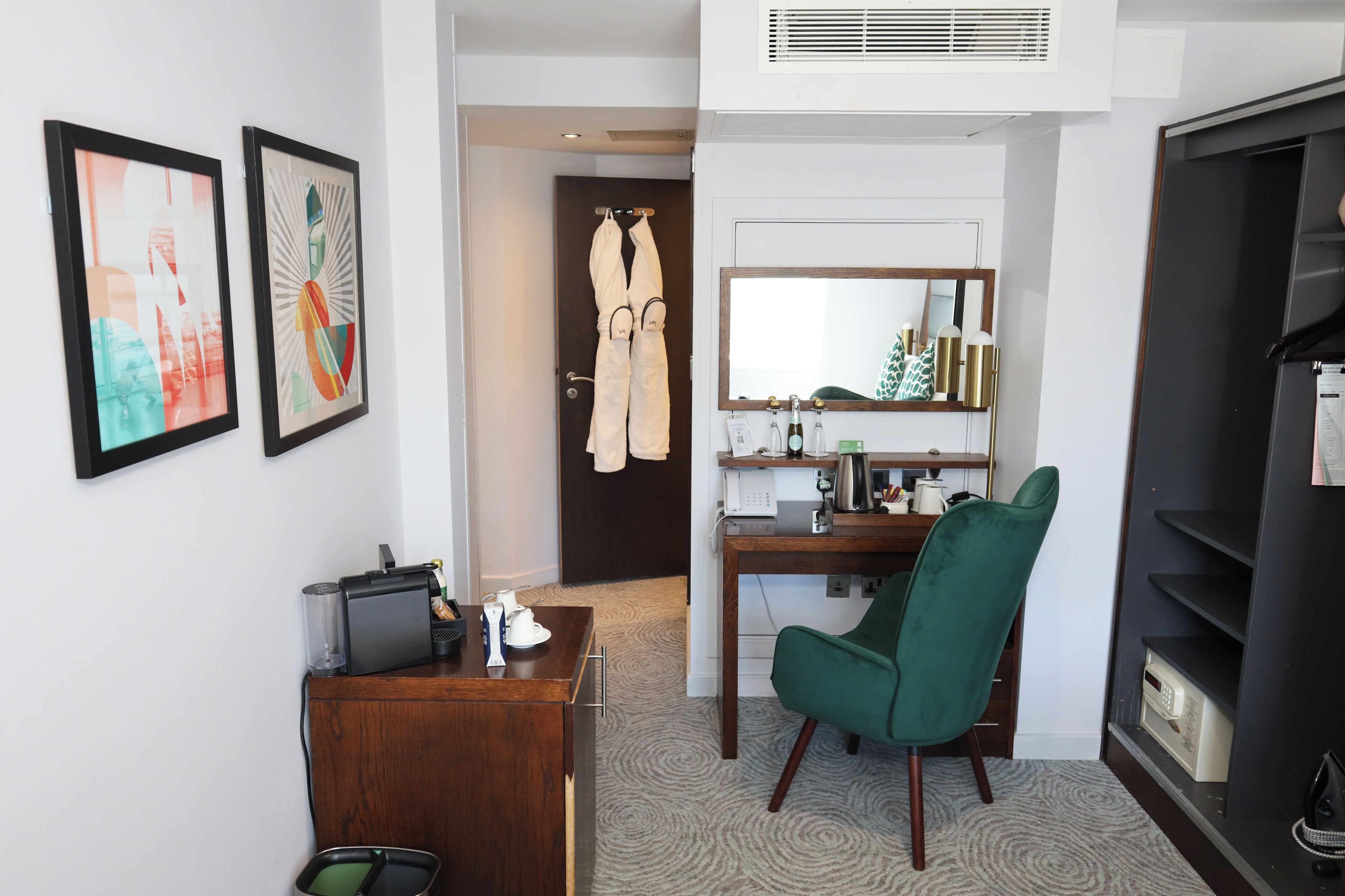 Una camera d'albergo con scrivania, sedia, minibar e opere d'arte appese al muro.