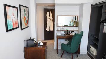 Una camera d'albergo con scrivania, sedia, minibar e opere d'arte appese al muro.