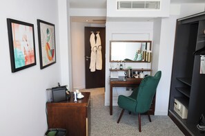 A hotel room with a desk, chair, minibar, and artwork on the wall. - Mercure London Paddington (London)