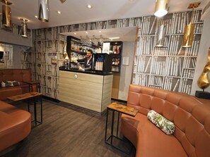 A bar area with a bartender, a seating area with sofas, and a wall with a patterned design. - Mercure London Paddington (London)