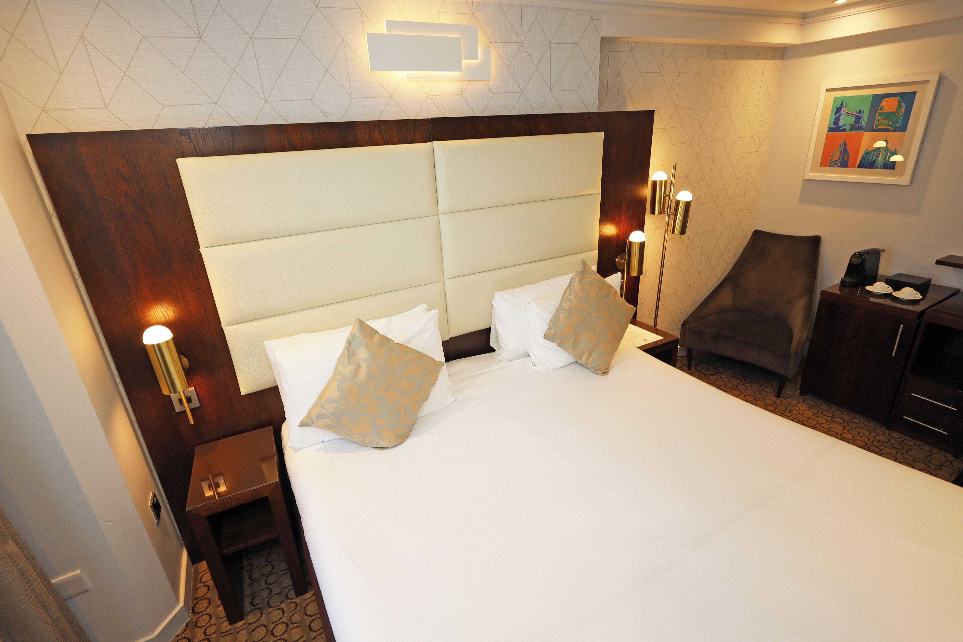 A hotel room with a large bed, bedside lamps, a chair, a desk, and a painting on the wall.