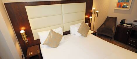 A hotel room with a large bed, bedside lamps, a chair, a desk, and a painting on the wall.