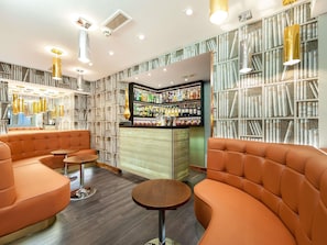 A bar area with bookshelves, orange seating, and a bar counter with various bottles.