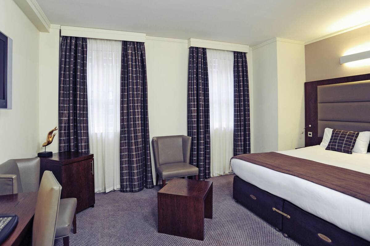 A hotel room with a bed, desk, chair, and a small table.