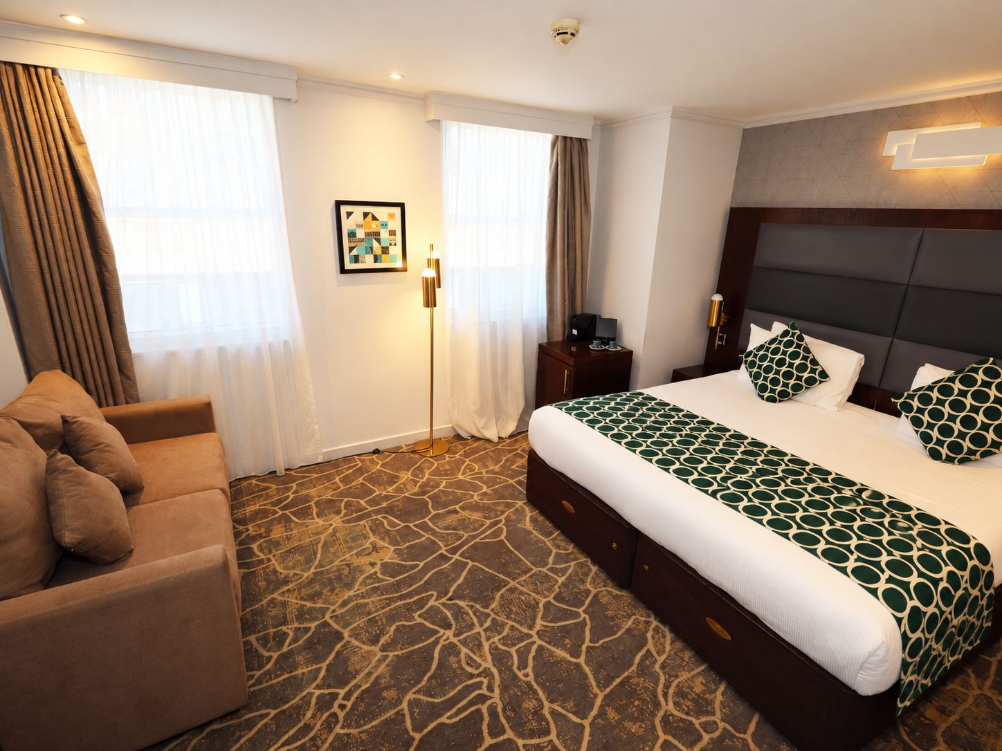 Una camera d'albergo con un letto, una poltrona, una scrivania e un quadro appeso al muro.