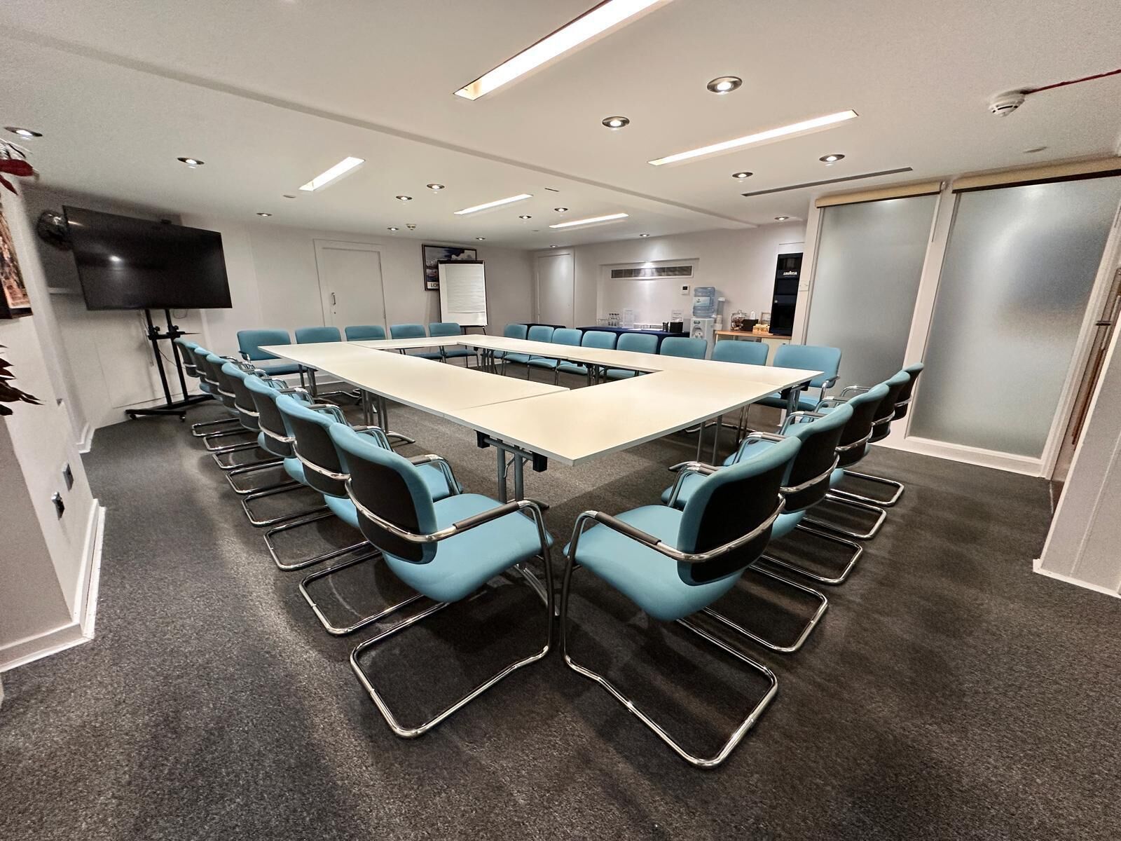 Une salle de conférence avec une longue table, des chaises bleues, un téléviseur à écran plat et un tableau blanc.
