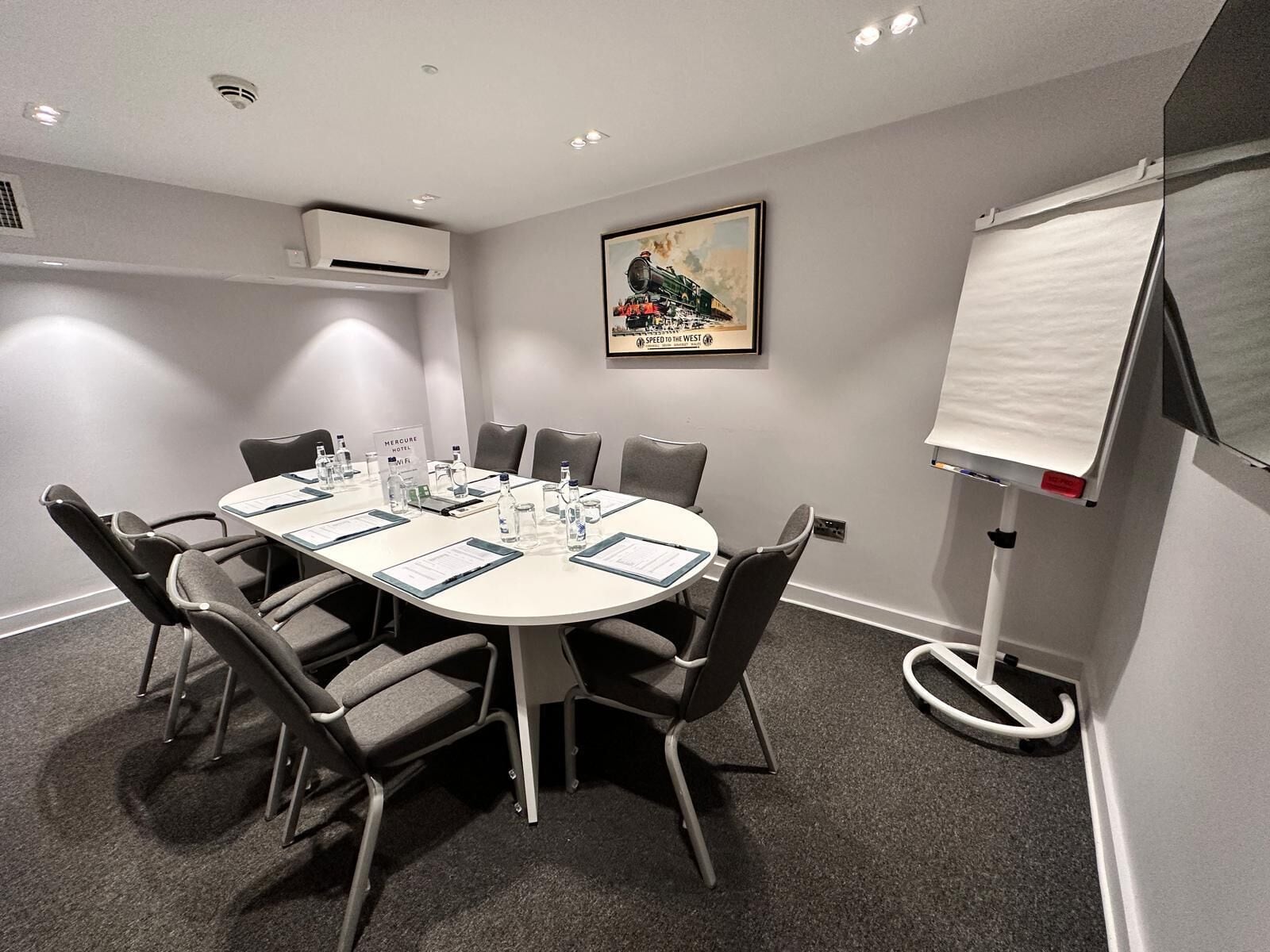 Een vergaderruimte met een ronde tafel, stoelen, een whiteboard en een lijstmuur met een ingelijste foto.